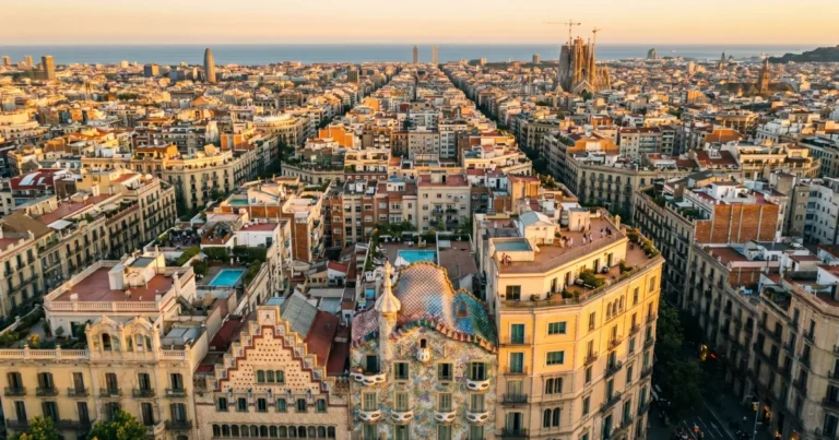 aerial view of Barcelona's Eixample grid at golden hour, rooftop terraces visible, Casa Batlló facade catching warm light in the foreground, wide urban sprawl meeting the sea in the distance