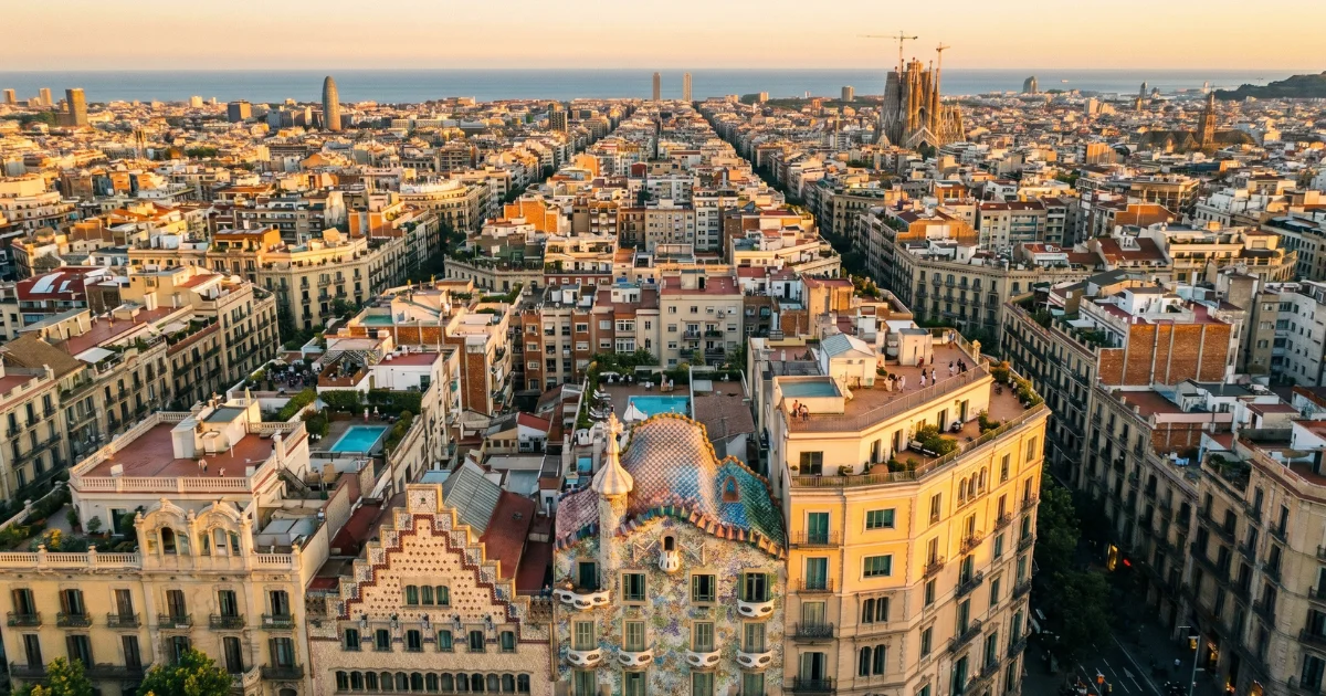 aerial view of Barcelona's Eixample grid at golden hour, rooftop terraces visible, Casa Batlló facade catching warm light in the foreground, wide urban sprawl meeting the sea in the distance